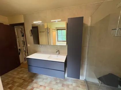 Salle de bain rénovée avec meuble suspendu bleu ardoise, vasque blanche, grand miroir éclairé et douche à l’italienne.